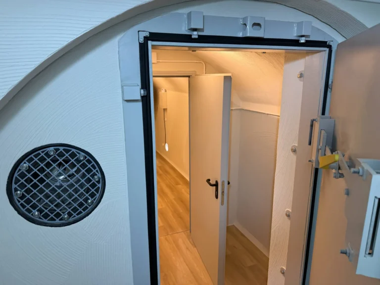 Open blast door of Revonia premium bomb shelter showing NBC ventilation filter and interior corridor with wooden floor – underground air-raid bunker for sale in Europe